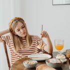 Teen girl in striped shirt at breakfast table with fruits, bread, and juice. Casual morning setting.