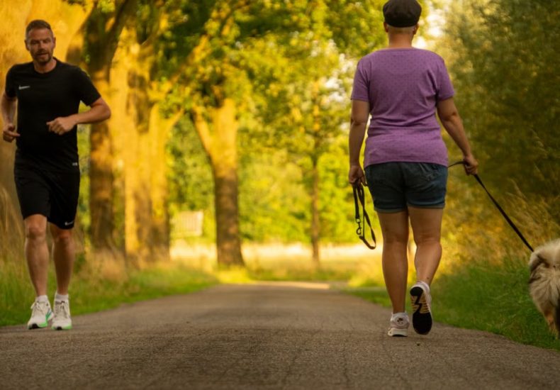 Man jogging and woman walking a dog on a picturesque outdoor path.